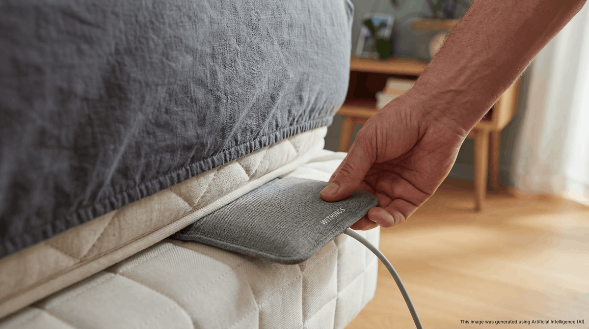 A Withings Sleep Mat sliding underneath a mattress